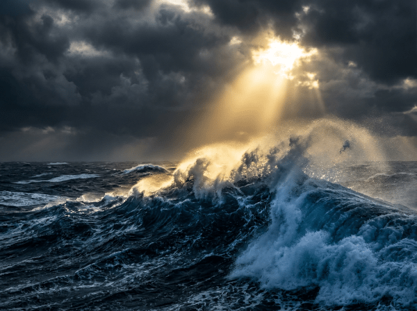 Sunlight breaking through storm clouds over crashing ocean waves